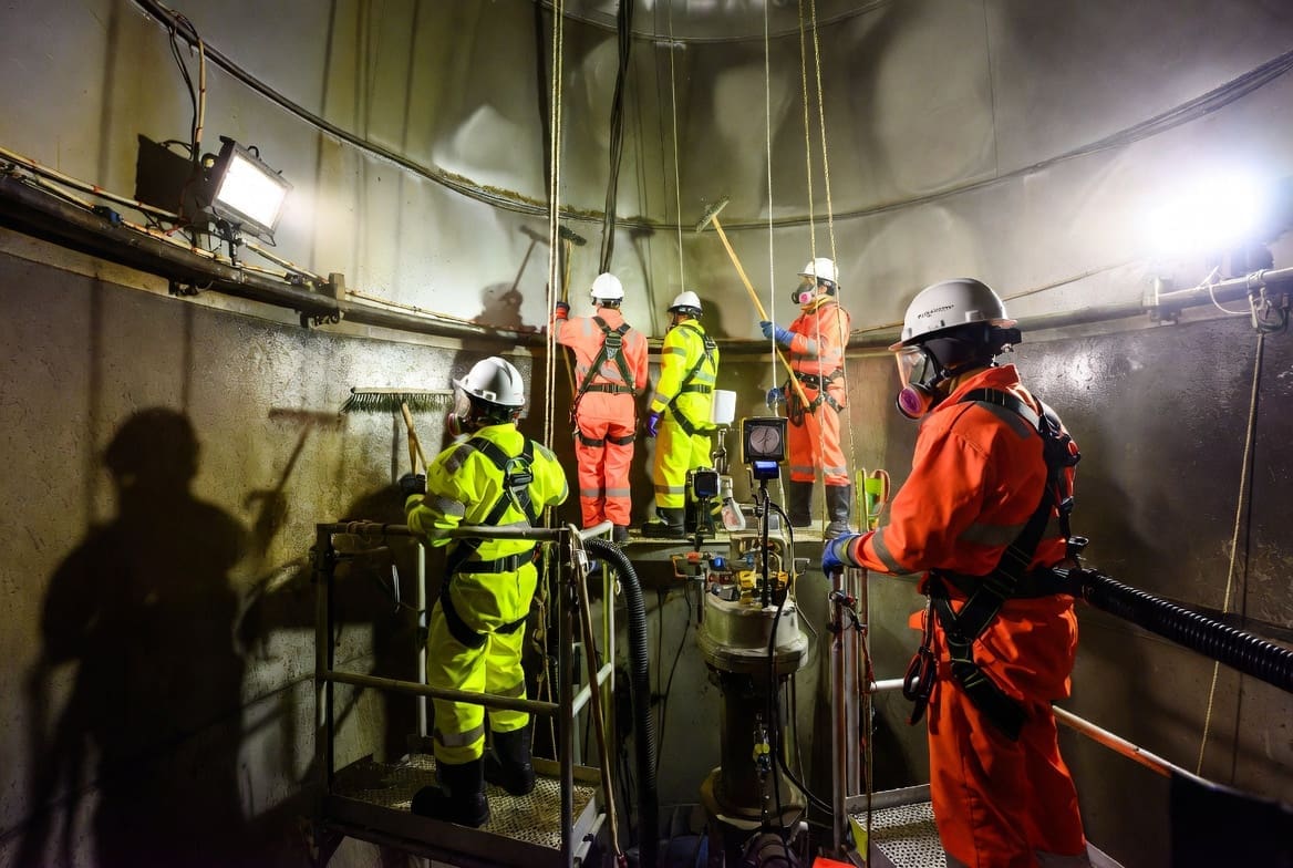 Professional team performing confined space tank cleaning inside a large industrial tank using proper PPE and safety equipment